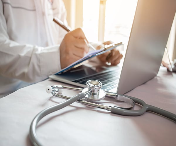 Medicine doctor's writing on laptop in medical office.Focus stethoscope on foreground table in hospital.